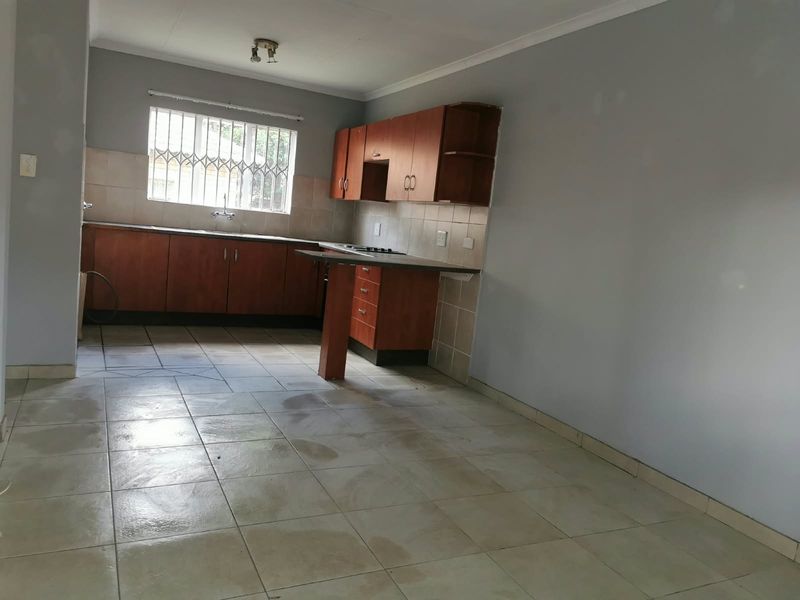 An empty kitchen featuring wooden cabinetry, tiled flooring, a built-in hob, and a window with security bars.