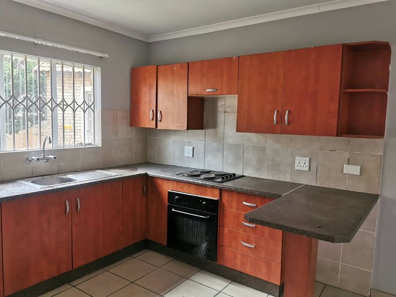 A functional kitchen featuring wood-look cabinetry, built-in oven and hob, tiled backsplash, and a breakfast nook counter, offering potential for modern updates.