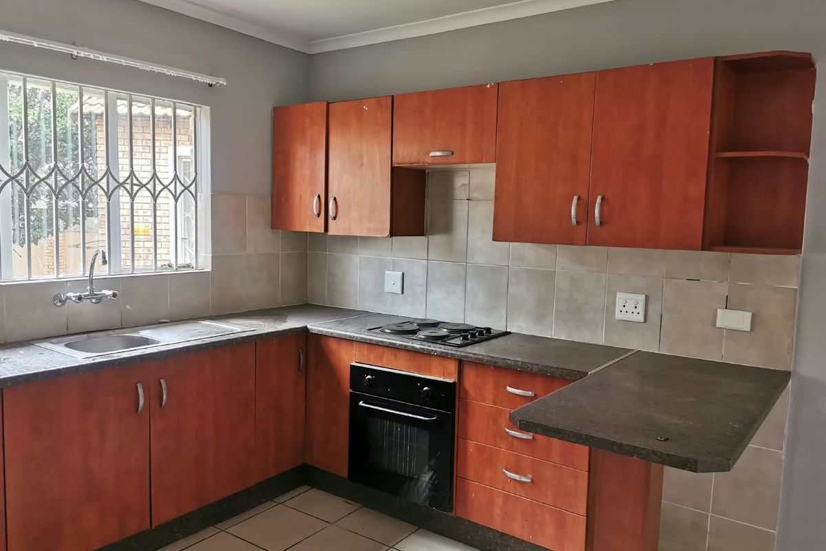 A functional kitchen featuring wood-look cabinetry, built-in oven and hob, tiled backsplash, and a breakfast nook counter, offering potential for modern updates.