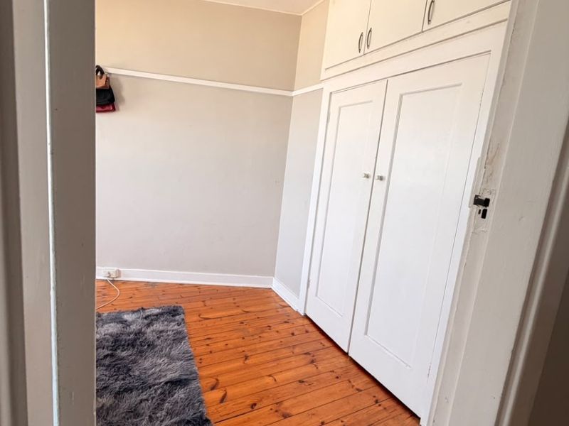 A bedroom featuring original timber flooring, built-in cupboards with overhead storage, and a classic picture rail.