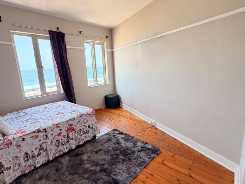 A bedroom featuring original hardwood flooring, picture rails, and dual windows offering a direct ocean view.