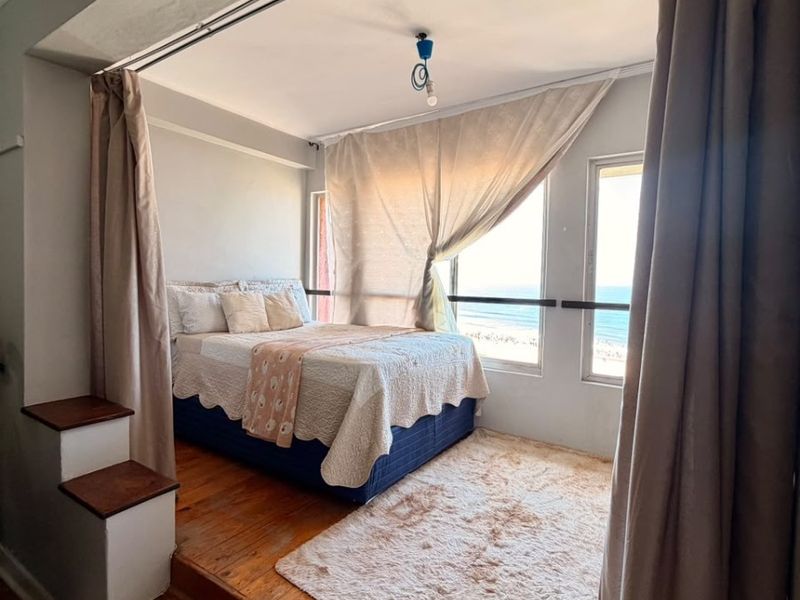 A bedroom featuring timber flooring, a raised platform area, and large windows offering ocean views.
