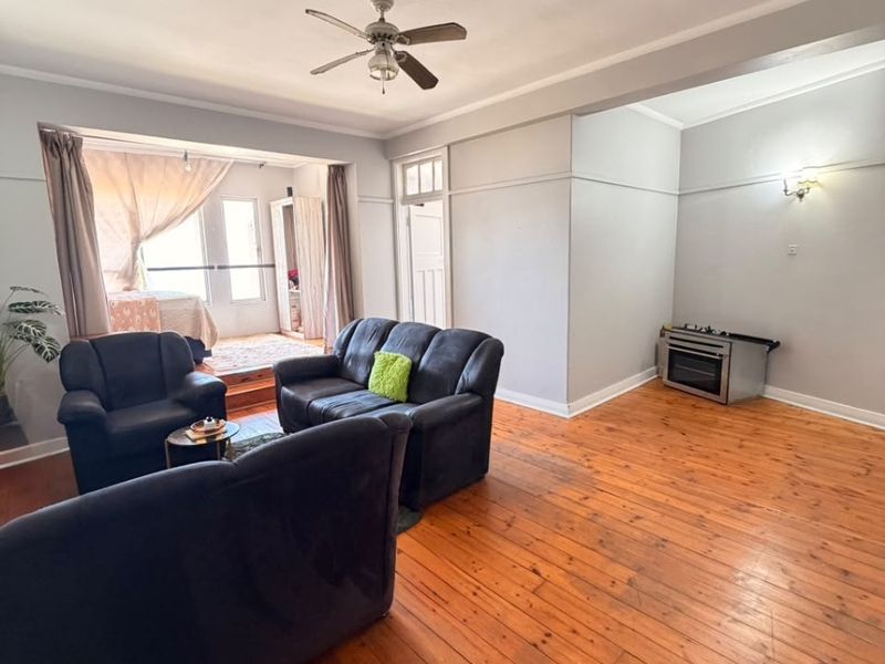 Open plan living area featuring polished hardwood flooring, a ceiling fan, and a freestanding oven, offering a versatile space with potential for modern updates.