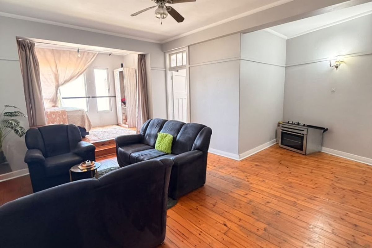Open plan living area featuring polished hardwood flooring, a ceiling fan, and a freestanding oven, offering a versatile space with potential for modern updates.