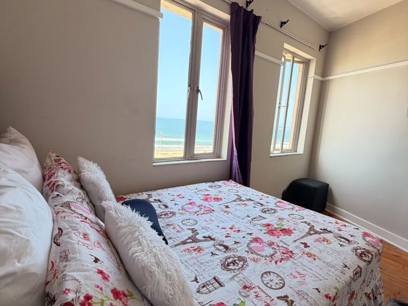 A bedroom featuring hardwood flooring, picture rails, and dual casement windows offering a direct view of the ocean.