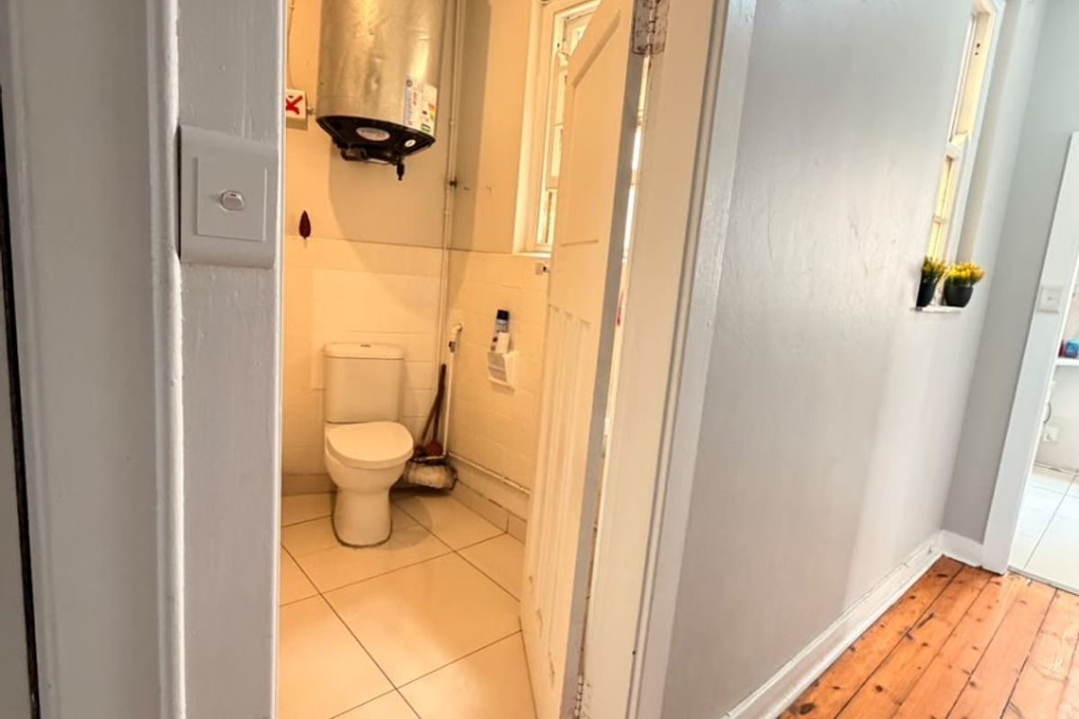A small bathroom featuring a toilet and an exposed electric water heater, accessible from a hallway with timber flooring.