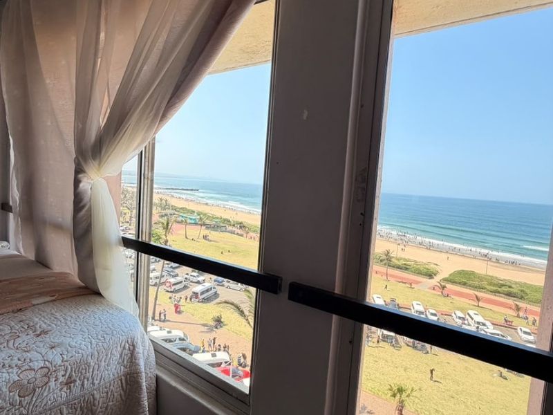 Bedroom featuring large windows with security bars, offering a direct view of the beach and coastal promenade.
