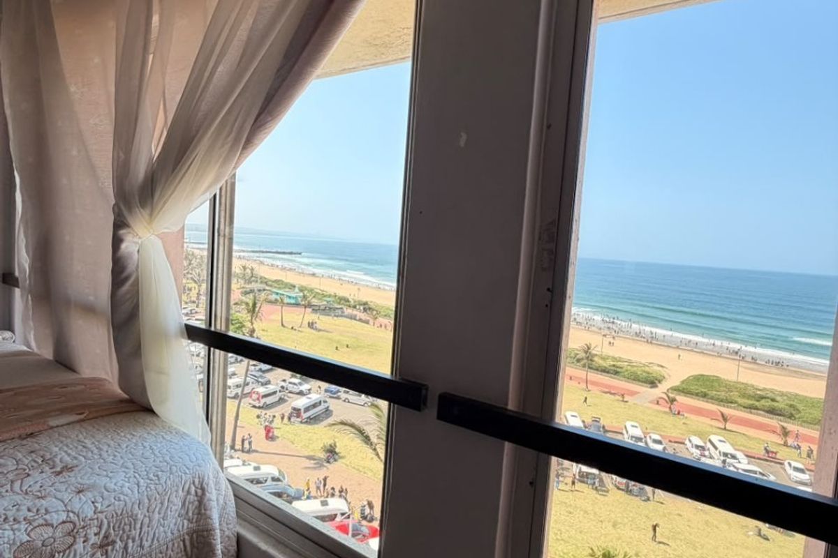 Bedroom featuring large windows with security bars, offering a direct view of the beach and coastal promenade.