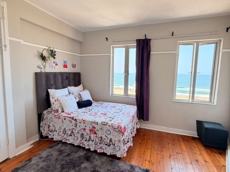 A bright bedroom featuring original hardwood flooring, picture rails, and dual windows offering expansive ocean views.