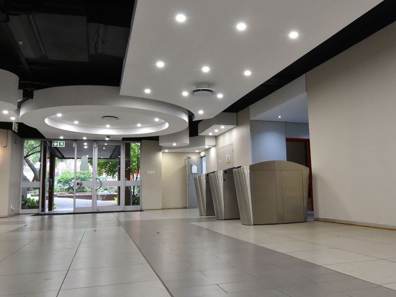 Modern commercial building entrance lobby featuring tiled flooring, recessed ceiling lighting, and integrated security turnstiles leading to the main access point.
