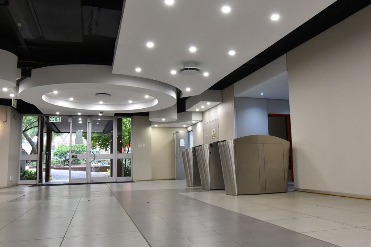 Modern commercial building entrance lobby featuring tiled flooring, recessed ceiling lighting, and integrated security turnstiles leading to the main access point.