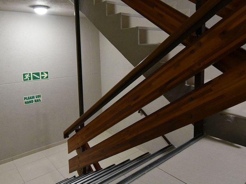 A functional commercial stairwell featuring a wooden handrail, tiled flooring, and clear emergency exit signage.