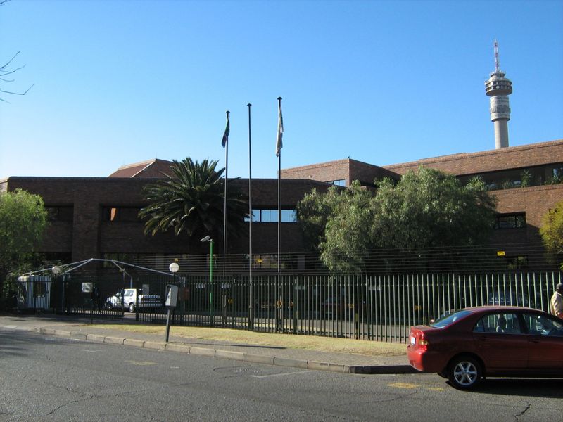 Front exterior view of a commercial brick office building featuring secure perimeter fencing, gated access, and flagpoles.