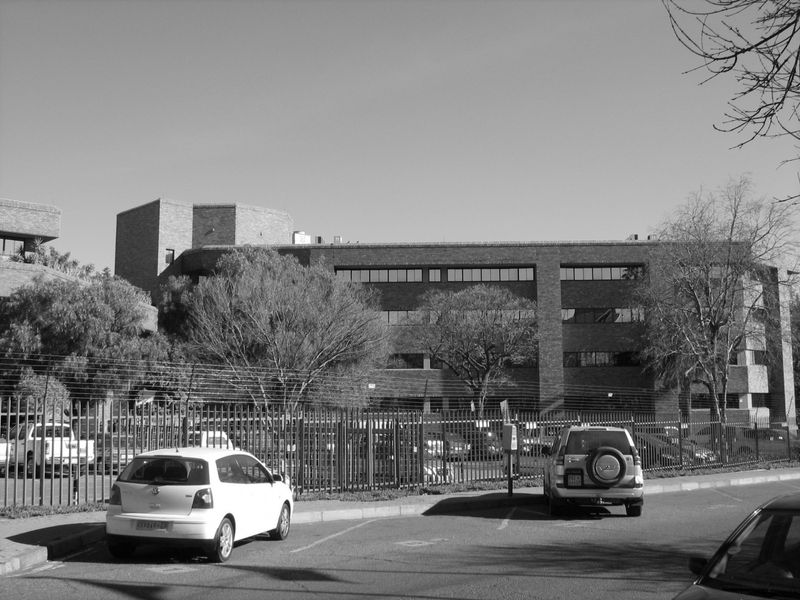 Exterior view of a multi-story commercial brick building featuring secure perimeter fencing and an adjacent paved parking area.