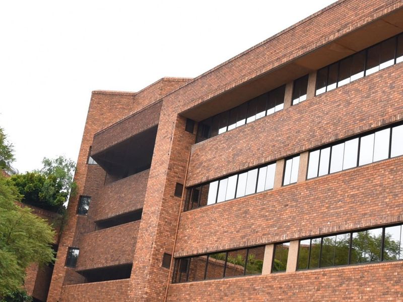 A multi-story commercial building featuring a classic red brick facade with integrated balconies and large, horizontal glass window panels.