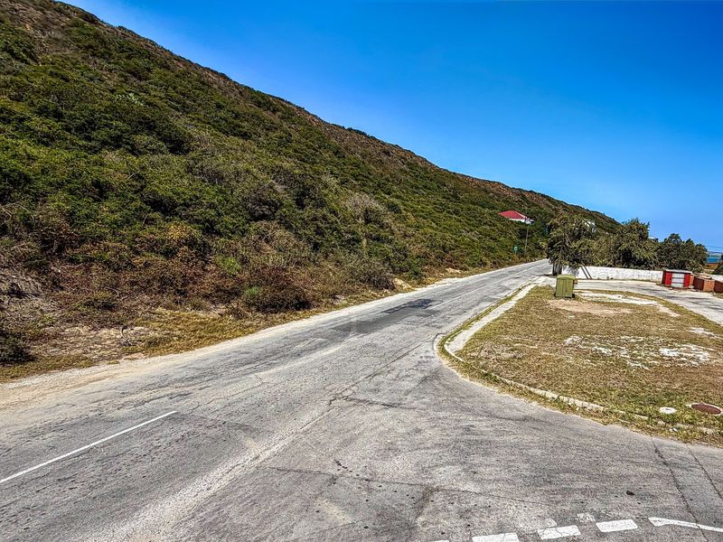 A view of the asphalt street and adjacent sloped hillside, showing the approach to the vacant residential land.