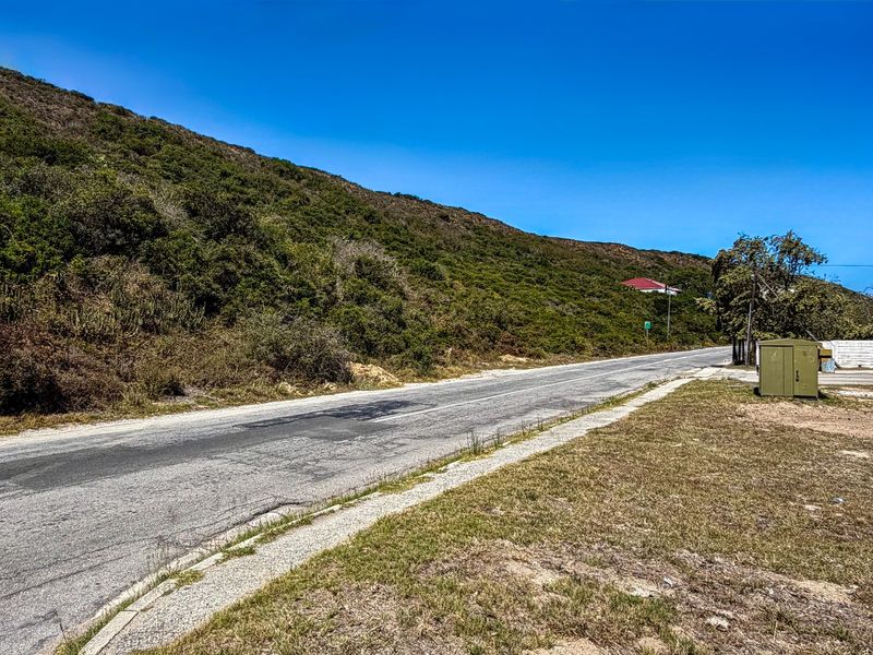 A view of the asphalt street and curb bordering the vacant residential land, featuring a hillside backdrop.