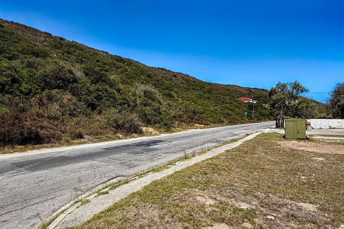 A view of the asphalt street and curb bordering the vacant residential land, featuring a hillside backdrop.