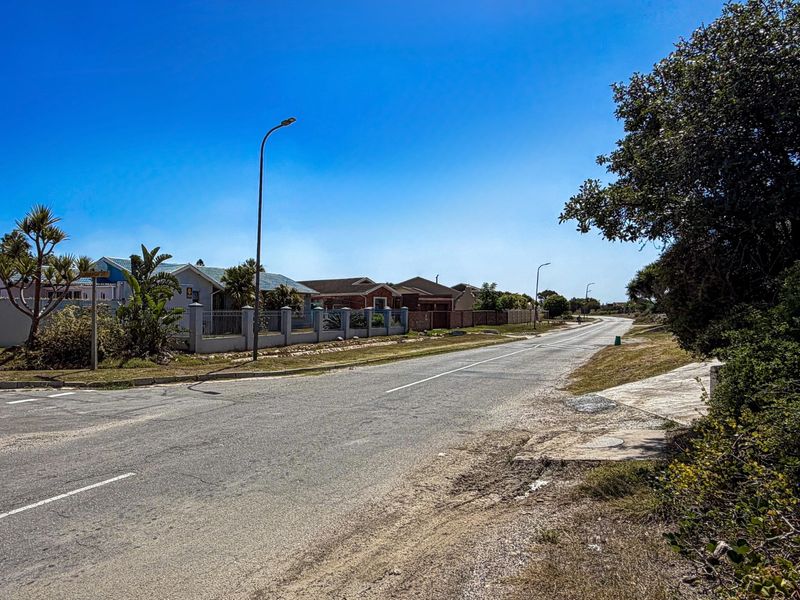 A clear street view showing the paved road, surrounding residential boundary walls, and established street lighting in a quiet neighborhood setting.