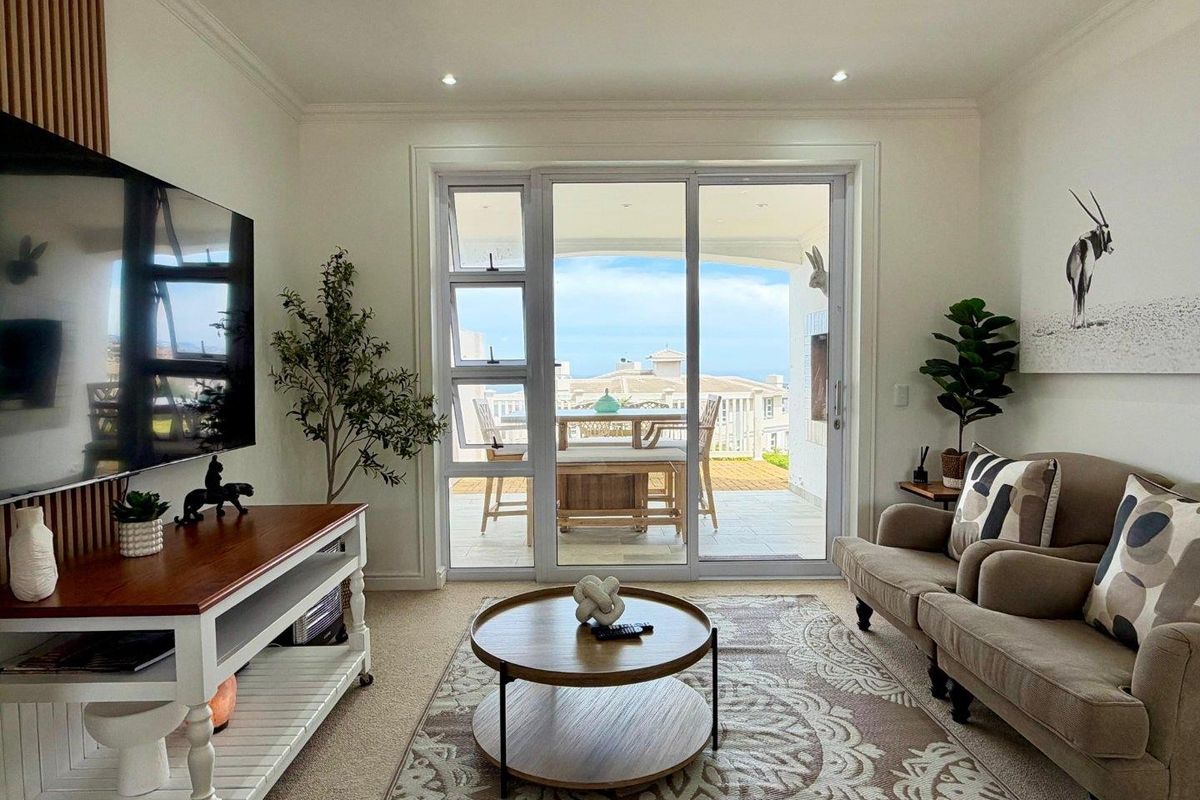 A well-maintained living room featuring a timber slat wall, recessed lighting, and large sliding glass doors that open onto a patio with coastal views.