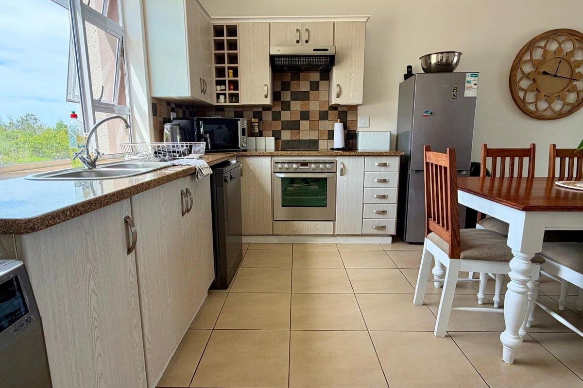 A functional kitchen featuring light wood-grain cabinetry, granite countertops, a tiled backsplash, and integrated appliances, with an adjacent dining area.
