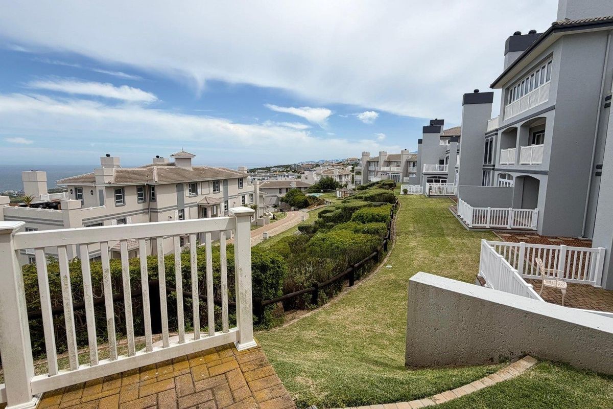 A view of the rear exterior of the townhouse complex, featuring paved patio areas, white railings, and well-maintained communal lawn and garden spaces.