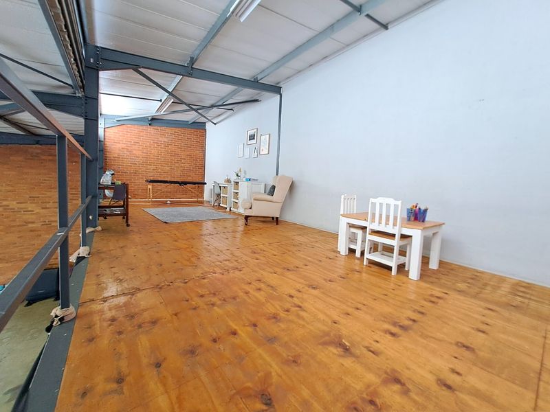 Spacious industrial-style mezzanine area featuring exposed steel structural beams, timber flooring, and a feature brick wall, offering versatile open-plan utility space.
