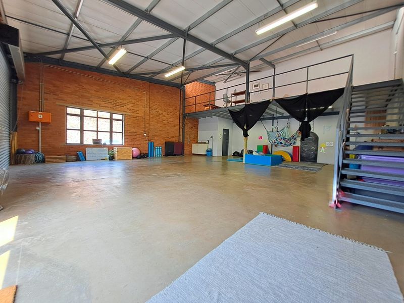 Spacious industrial utility area featuring exposed brick walls, high steel truss ceilings, a mezzanine level with metal staircase, and durable concrete flooring.