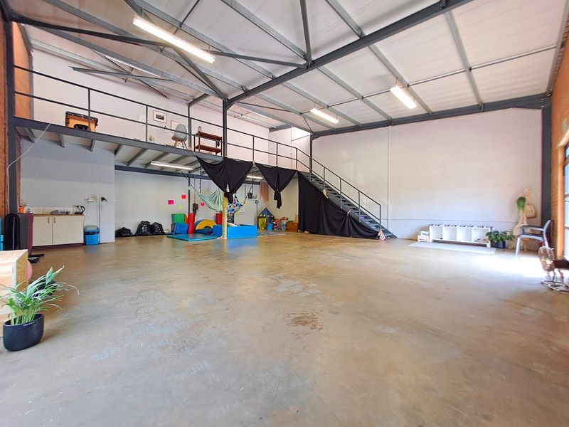 Spacious industrial utility area featuring a mezzanine level, steel staircase, exposed roof trusses, and concrete flooring, suitable for various commercial or workshop uses.
