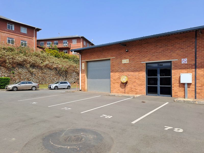 Industrial unit exterior featuring a brick facade, roller shutter door, glass entrance, and dedicated asphalt parking bays.
