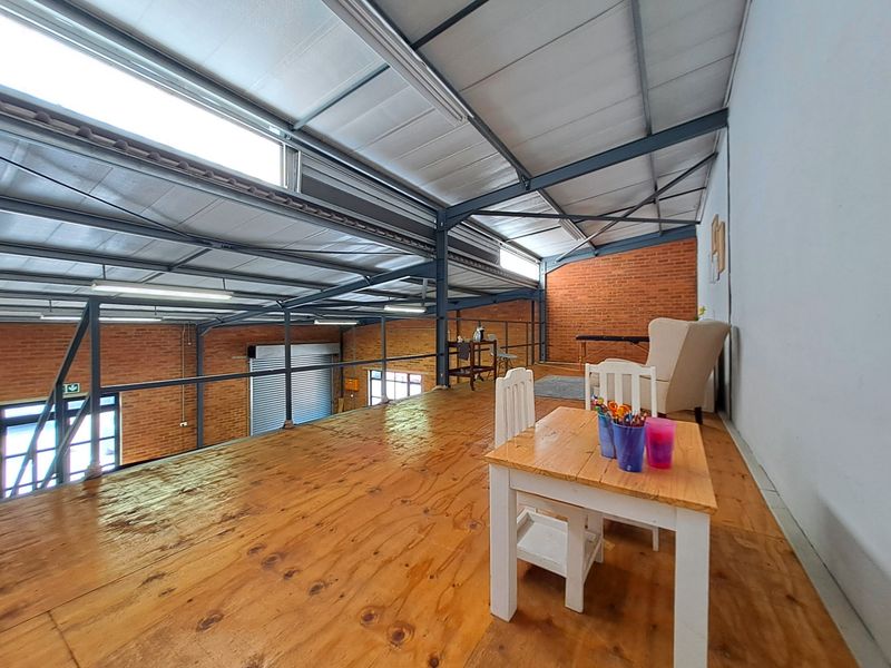 Spacious industrial-style mezzanine level featuring exposed brickwork, steel roof trusses, and timber flooring, overlooking the main warehouse area.