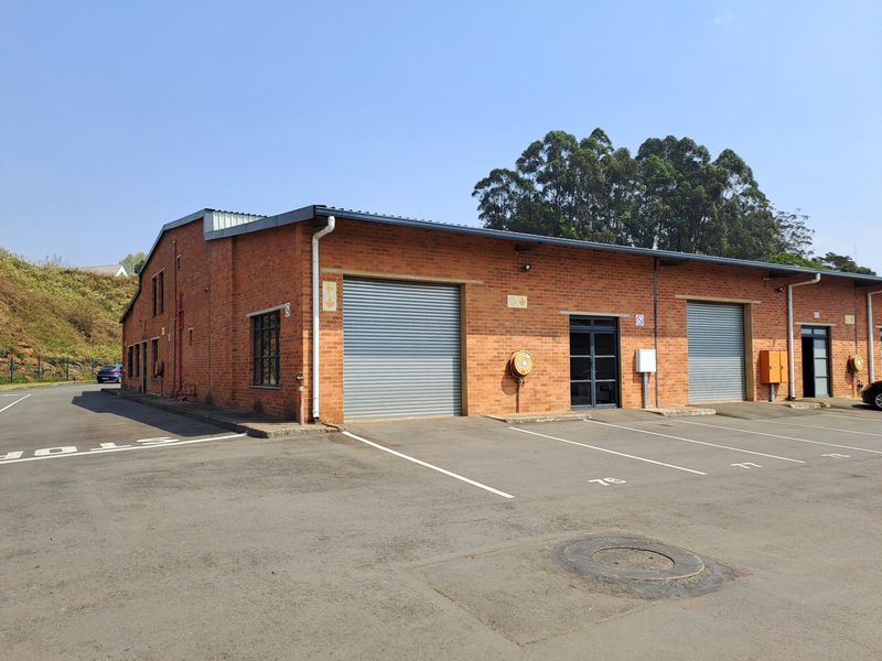 Industrial warehouse building featuring a red brick facade, multiple roller shutter doors, and dedicated asphalt parking bays.