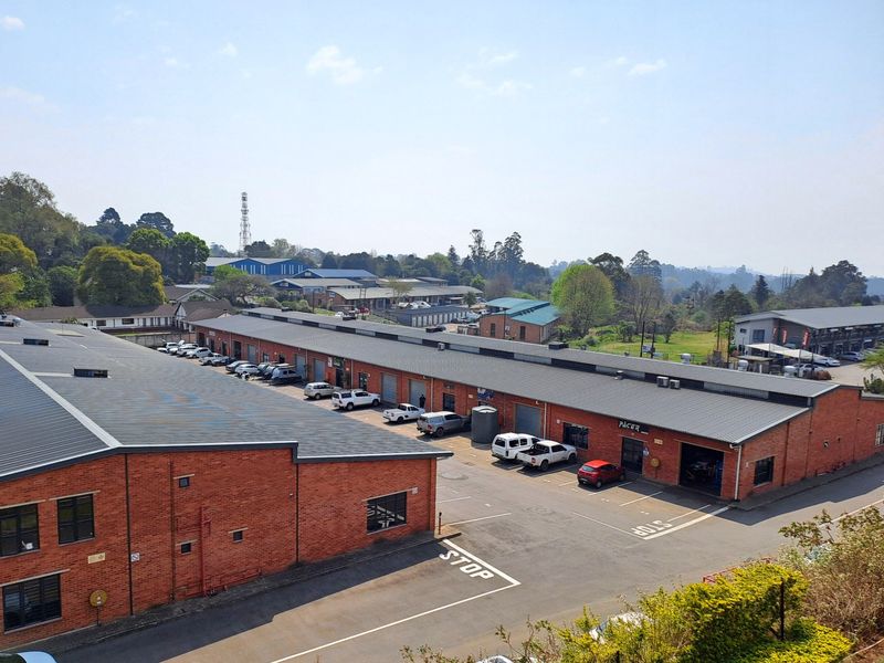 Aerial view of an industrial complex featuring multiple brick warehouse units with corrugated metal roofs and dedicated asphalt parking areas.