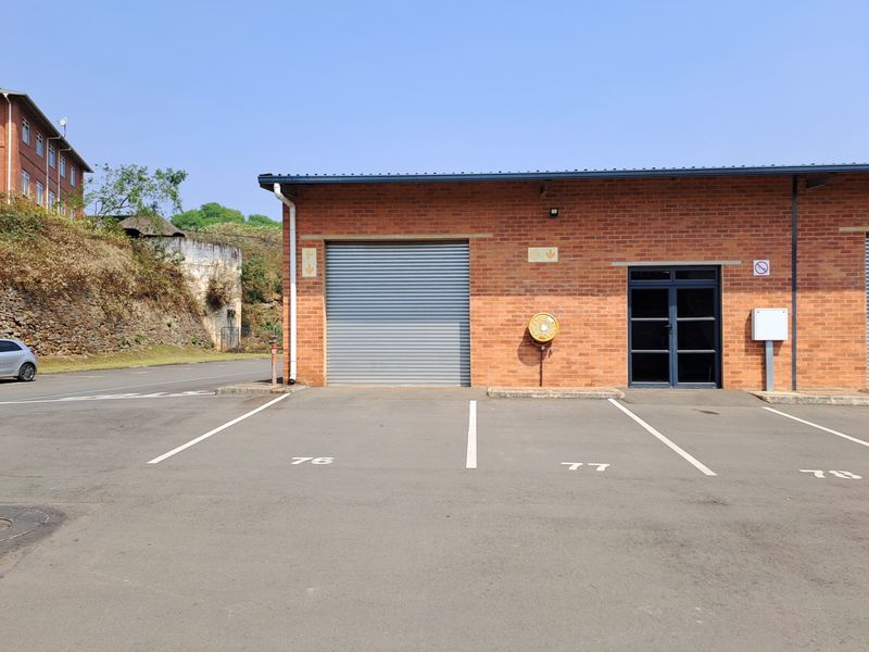 Industrial unit exterior featuring a roller shutter door, glass entrance, and designated asphalt parking bays in a well-maintained brick building.