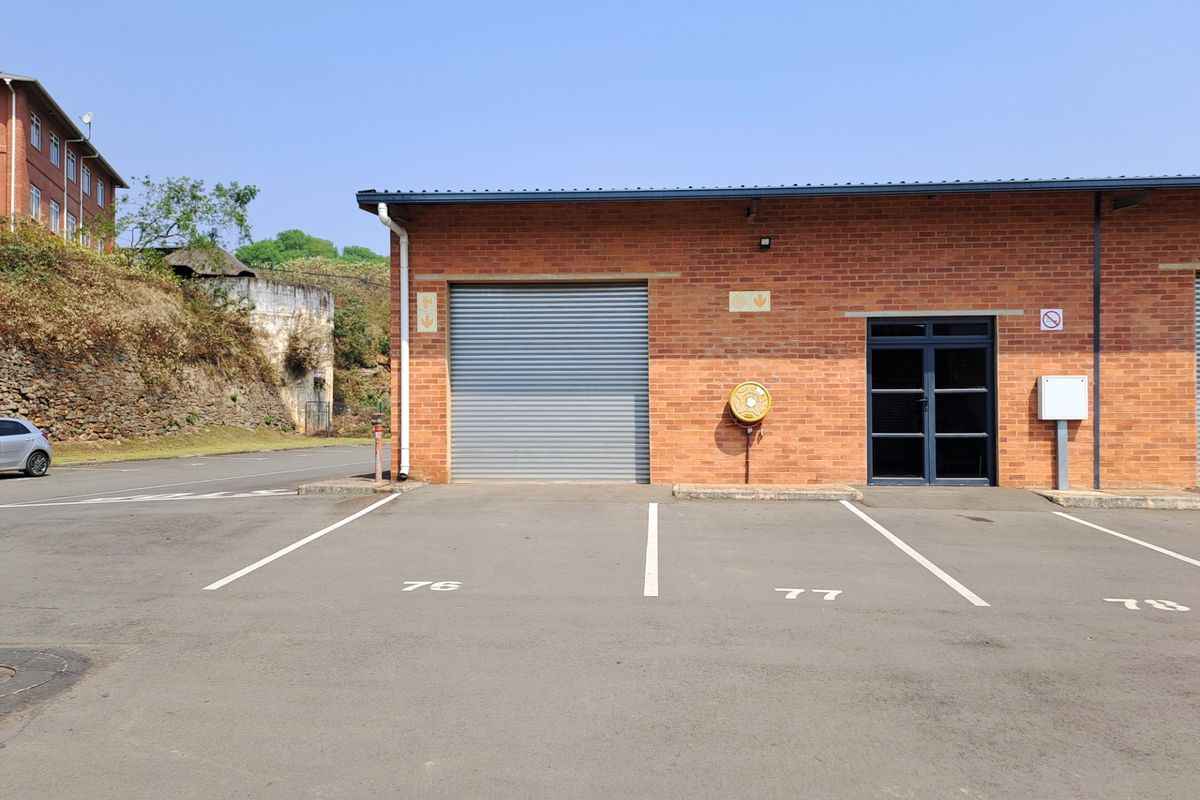 Industrial unit exterior featuring a roller shutter door, glass entrance, and designated asphalt parking bays in a well-maintained brick building.