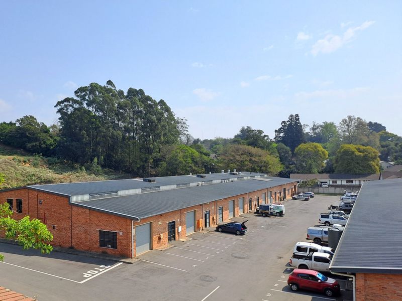 Aerial view of an industrial complex featuring brick warehouse buildings with metal roofing, roller shutter doors, and an expansive asphalt parking area.
