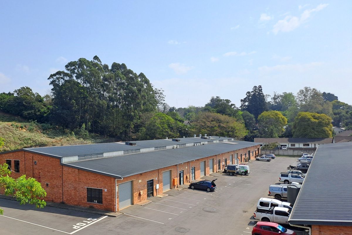 Aerial view of an industrial complex featuring brick warehouse buildings with metal roofing, roller shutter doors, and an expansive asphalt parking area.