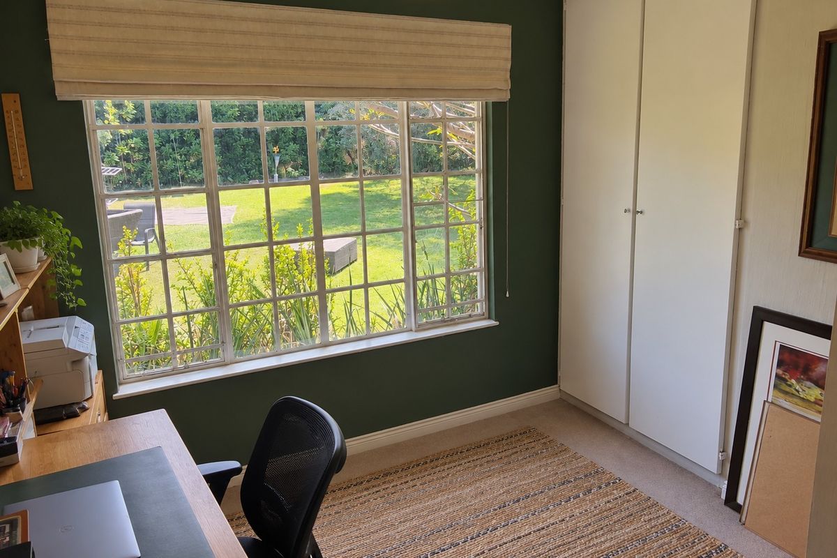 A well-lit bedroom featuring built-in cupboards, a large grid-pattern window overlooking the garden, and neutral carpeting.