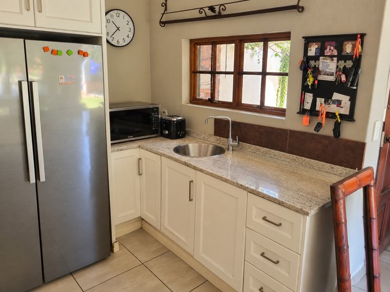 A functional kitchen area featuring granite countertops, shaker-style cabinetry, an undermount sink, and a tiled backsplash with a timber-framed window.