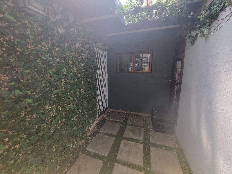 A covered outdoor patio area featuring paved flooring, a security gate, and a timber-framed window, offering a private and sheltered space.
