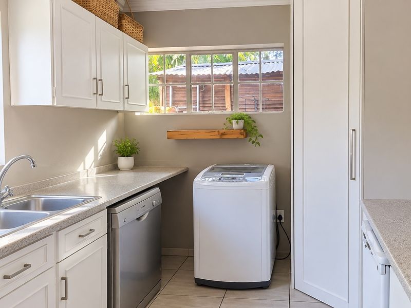 A well-maintained laundry area featuring white built-in cabinetry, a double sink, laminate countertops, and tiled flooring with ample storage space.