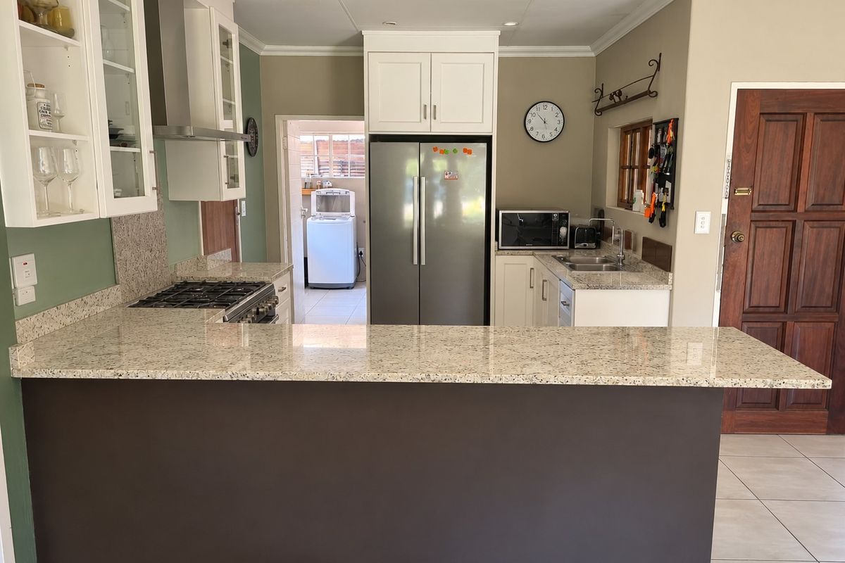 Well-appointed kitchen featuring granite countertops, gas hob, extractor fan, and ample built-in cabinetry, with a convenient breakfast bar and adjacent laundry area.