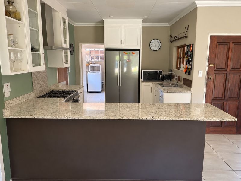 Well-appointed kitchen featuring granite countertops, gas hob, extractor fan, and ample built-in cabinetry, with a convenient breakfast bar and adjacent laundry area.