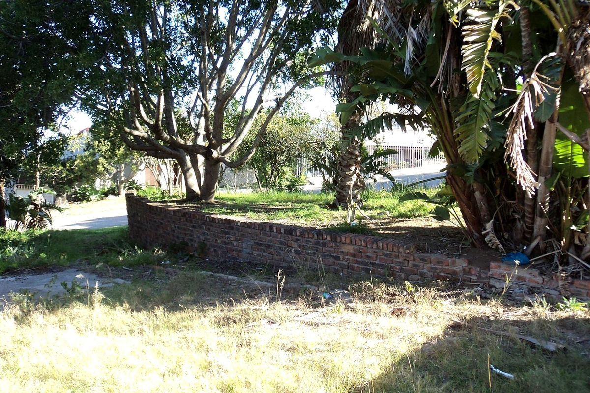 A view of a residential garden area featuring mature trees and a brick retaining wall on a vacant land plot.