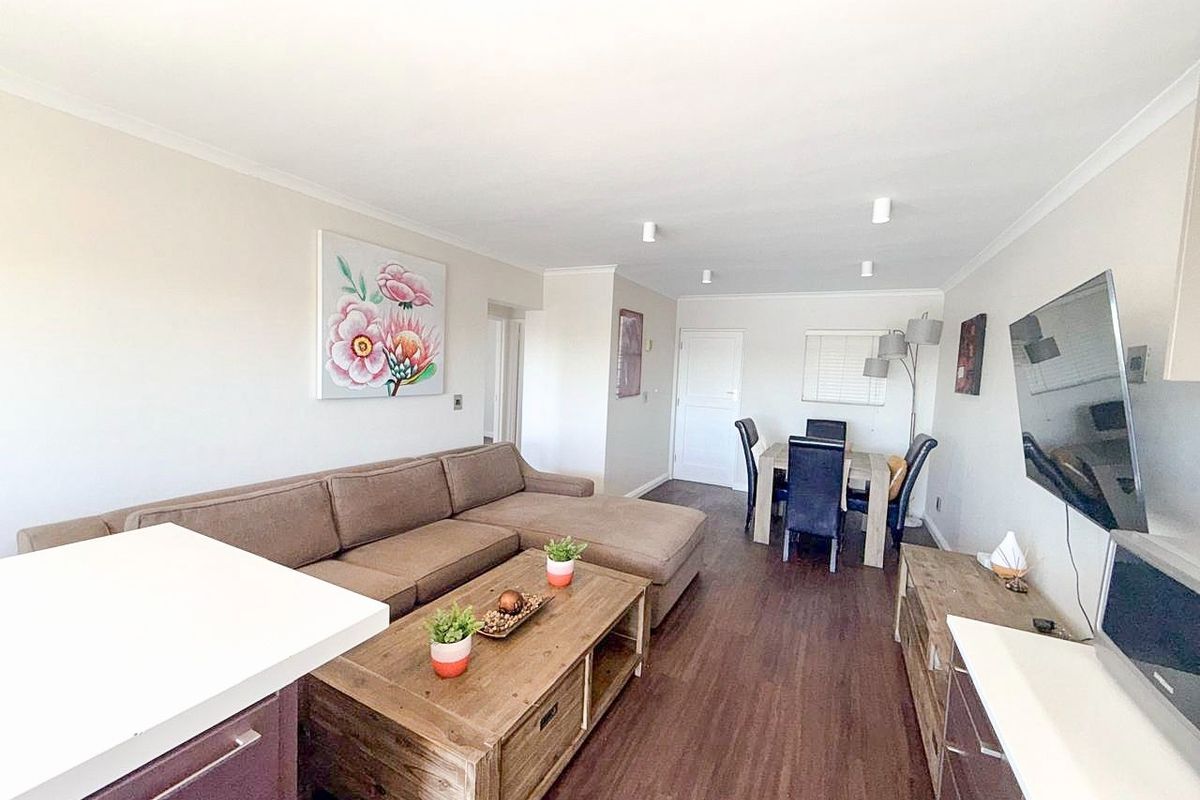 An open-plan living and dining area featuring laminate flooring, neutral walls, and recessed ceiling lighting, creating a functional and cohesive living space.