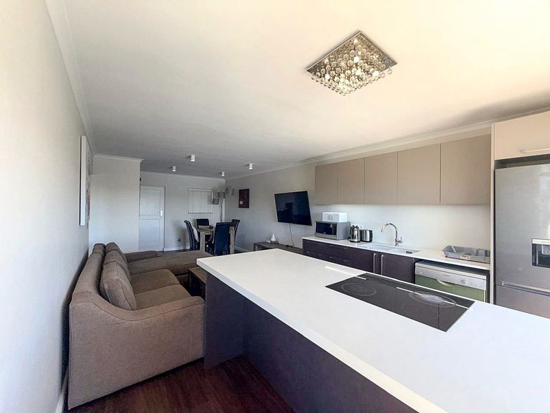 Modern open-plan living area featuring a sleek kitchen with a central island, integrated hob, and ample cabinetry, seamlessly flowing into the dining and lounge space.