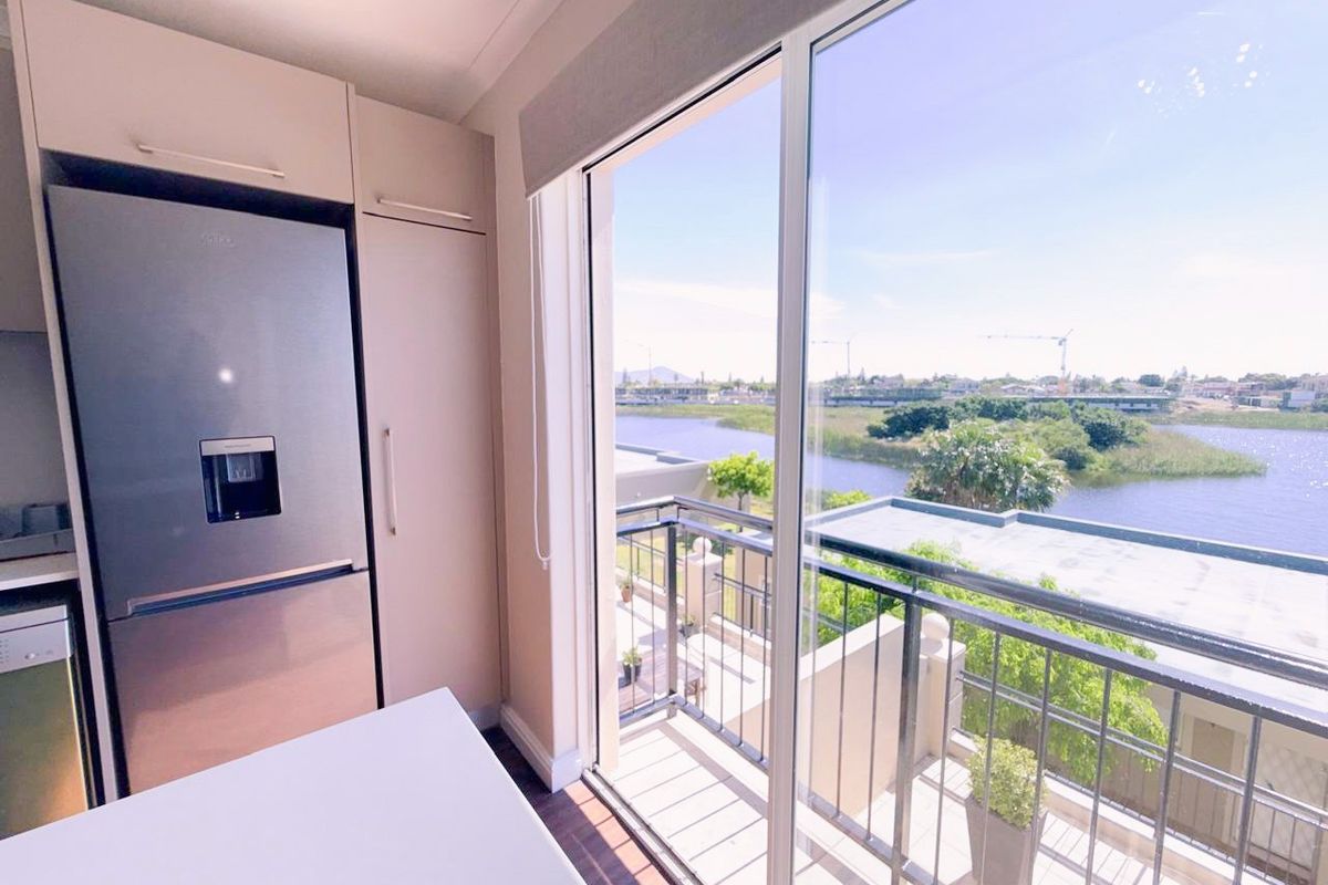 Modern kitchen area featuring sleek built-in cabinetry and an integrated refrigerator, with direct access to a balcony offering scenic water views.