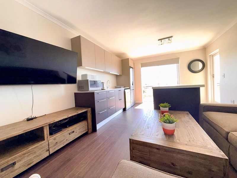 An open-plan living and kitchen area featuring modern cabinetry, laminate flooring, and a breakfast bar, leading to an outdoor balcony space.