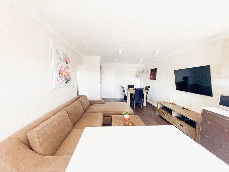 An open-plan living and dining area featuring laminate flooring and neutral wall finishes, providing a versatile space for relaxation and entertaining.