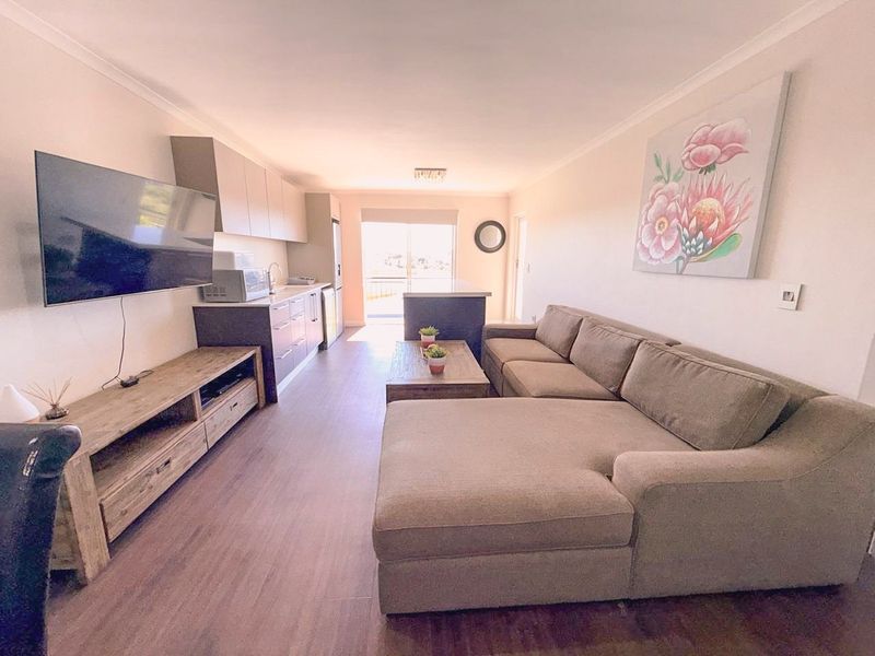 Open-plan living area featuring a compact kitchen with built-in cabinetry and laminate flooring, leading to a sliding glass door with natural light.